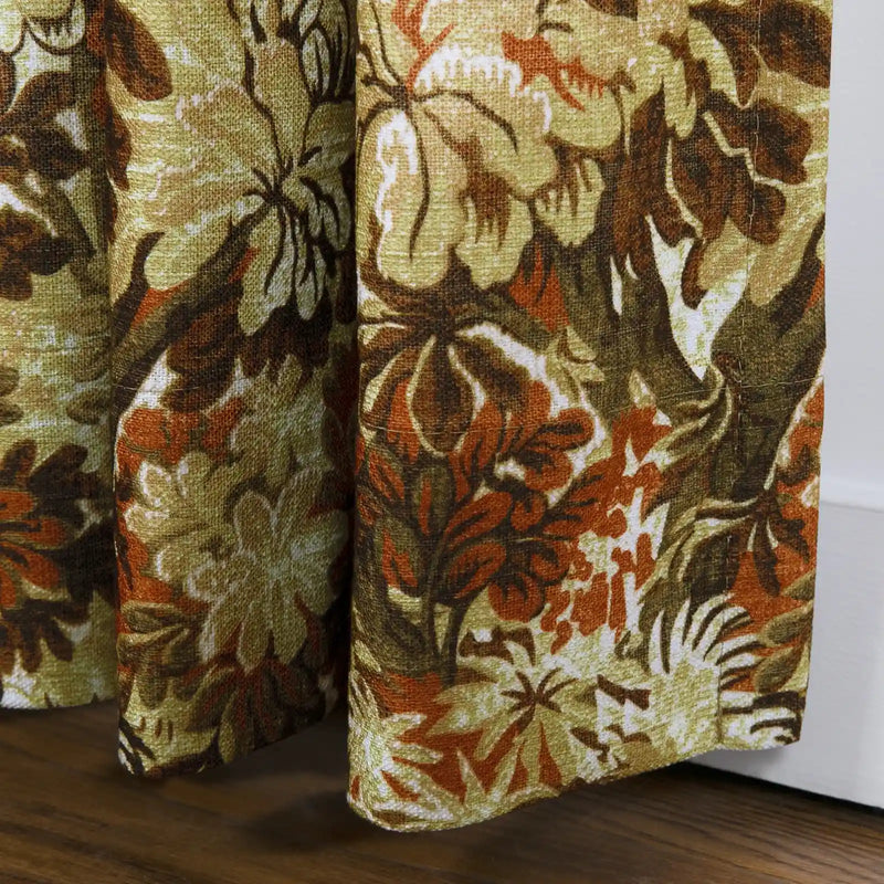 Textile curtains featuring a vintage botanical pattern of olive green, warm brown, and burnt orange rest on a dark wood floor next to a white baseboard