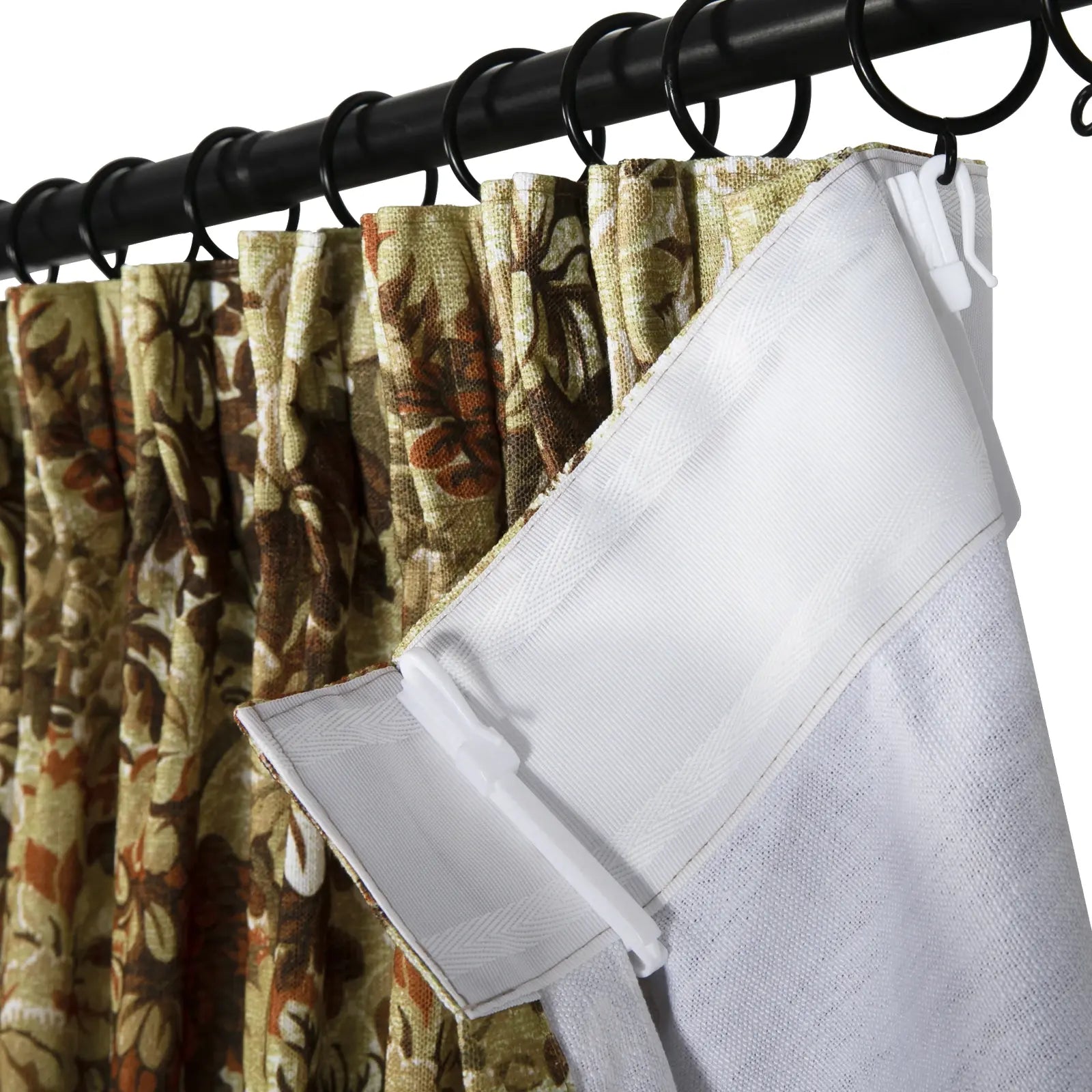 Close-up of brown and green floral patterned pleated curtains hanging from a black rod with black rings and white plastic hooks revealing a white fabric lining