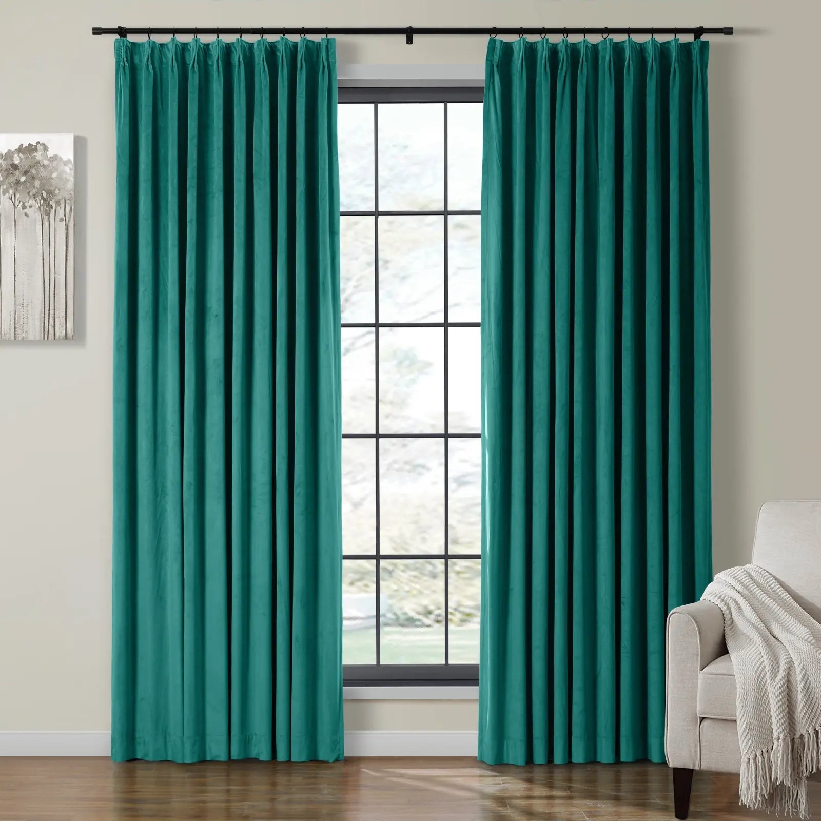 Pleated teal velvet curtains frame a black grid window in a room featuring an abstract tree painting and a cream armchair with a fringed throw