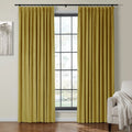 Photograph of a modern room featuring vibrant chartreuse velvet pleated curtains on a black rod, flanking a grid-paned window, alongside abstract grey tree artwork and a white armchair with a cream knitted throw