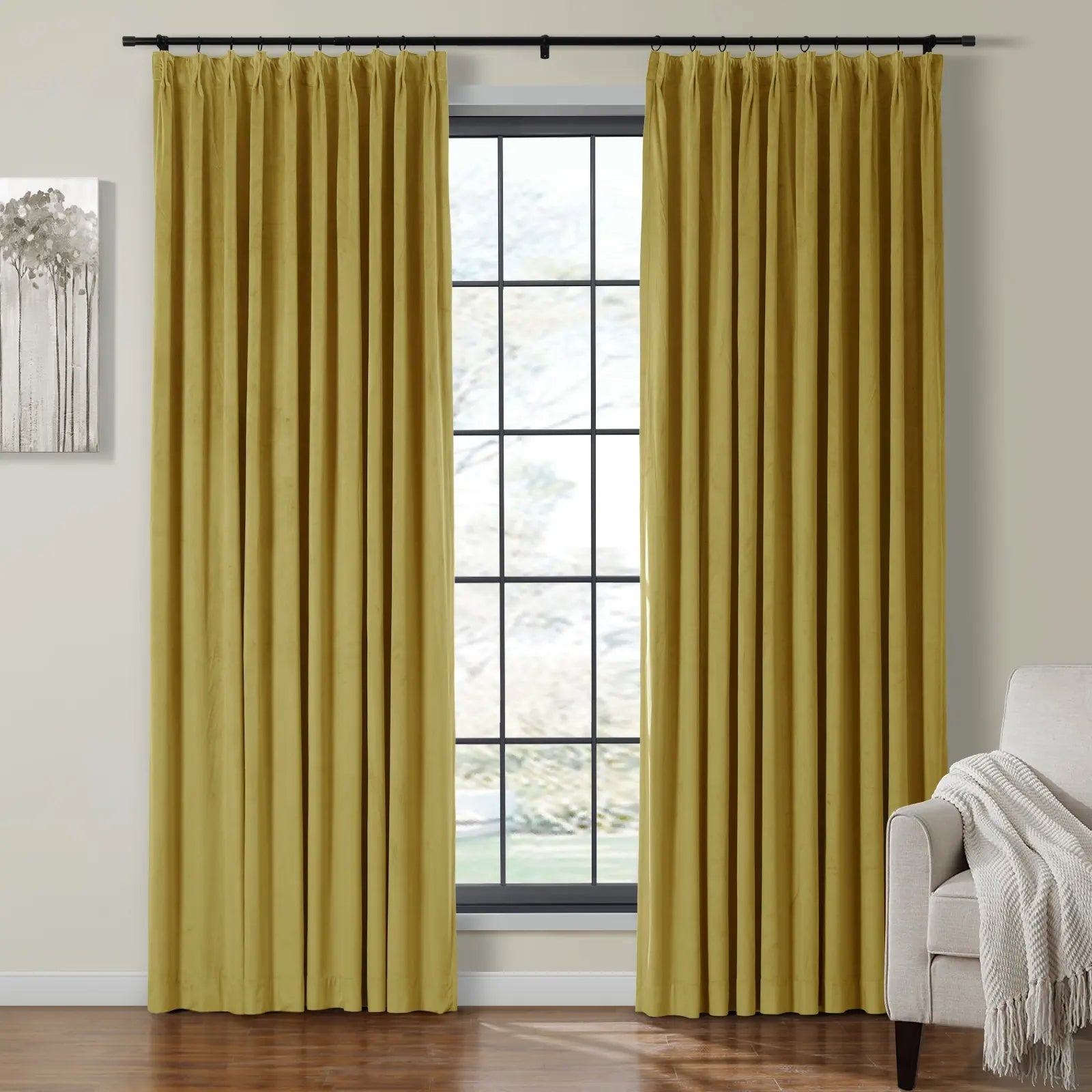 Photograph of a modern room featuring vibrant chartreuse velvet pleated curtains on a black rod, flanking a grid-paned window, alongside abstract grey tree artwork and a white armchair with a cream knitted throw