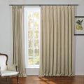 Beige textured draperies on a black rod frame a multi-pane window revealing a lush green outdoor view, complemented by an elegant white upholstered armchair with dark wood trim and a vibrant yellow lemon botanical print