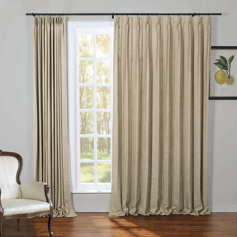 Beige textured draperies on a black rod frame a multi-pane window revealing a lush green outdoor view, complemented by an elegant white upholstered armchair with dark wood trim and a vibrant yellow lemon botanical print