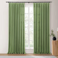 Sage green linen-look pinch-pleat curtains on a black rod covering a multi-paned window, next to a fluted wooden table with a black vase and candle holder