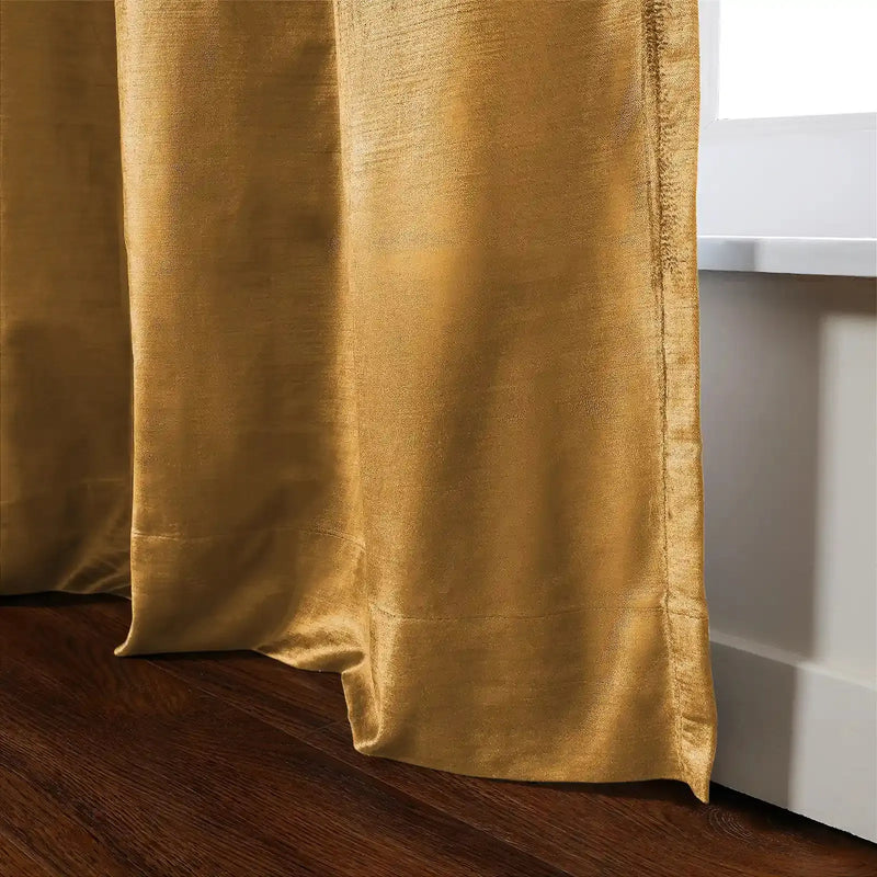 Golden yellow curtain of lustrous slub-textured fabric with cascading folds resting on a dark wood floor next to a white window frame