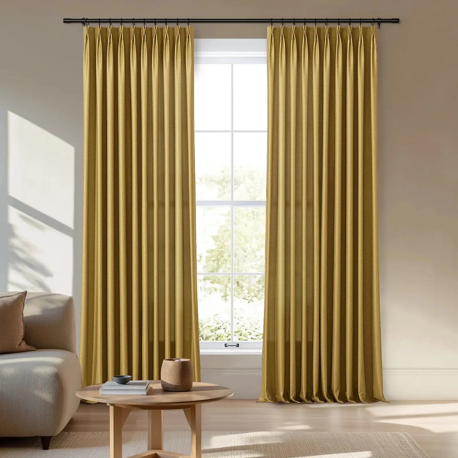 Floor-length golden pinch pleat curtains framing a window in a sunlit living room with a beige sofa and a light wood coffee table holding books and a pot