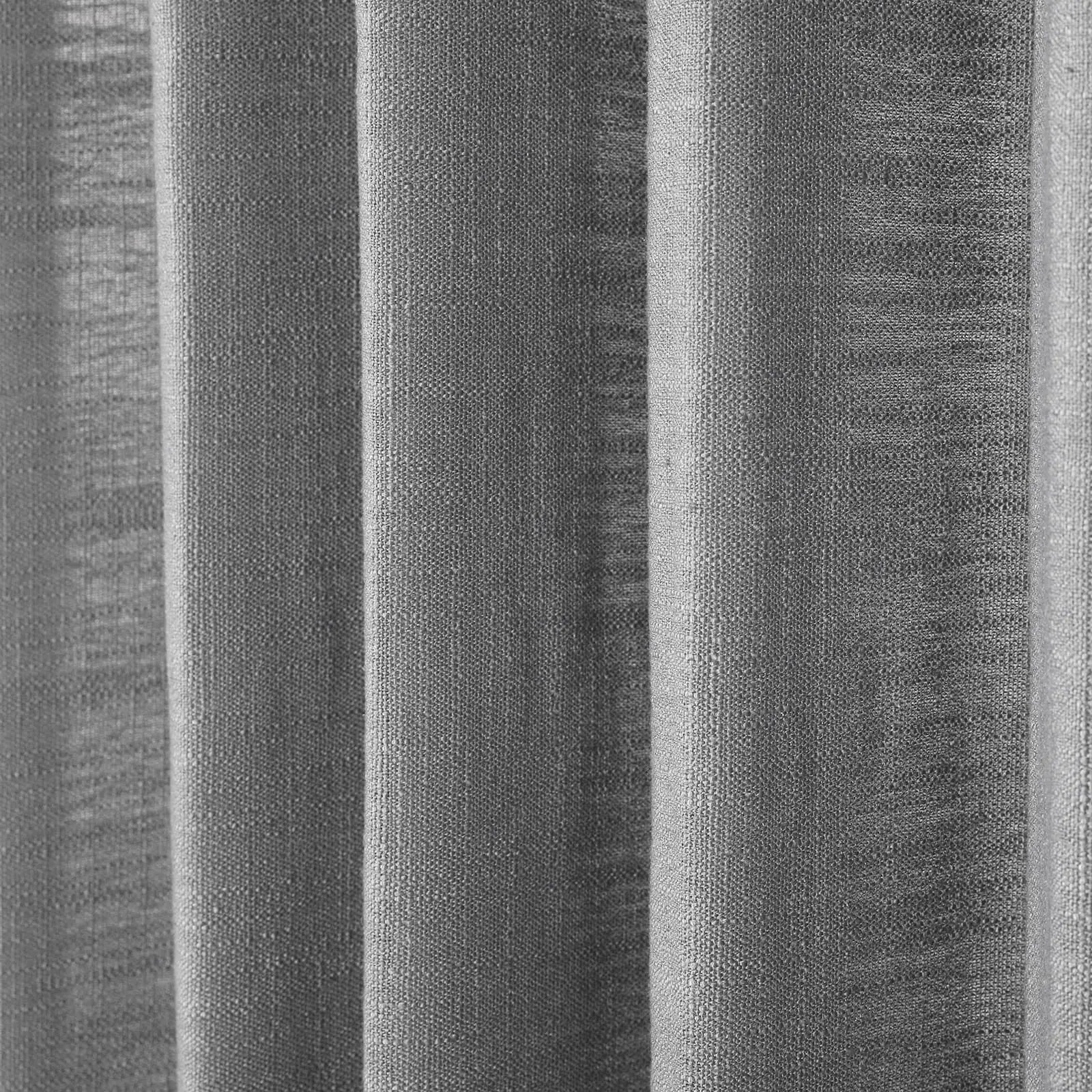 Photograph of a light grey woven fabric displaying prominent vertical pleats with visible coarse texture and subtle shifts in monochromatic tone