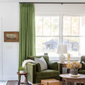 Green Liz linen curtains shown closer beside a sunlit window with smooth vertical folds