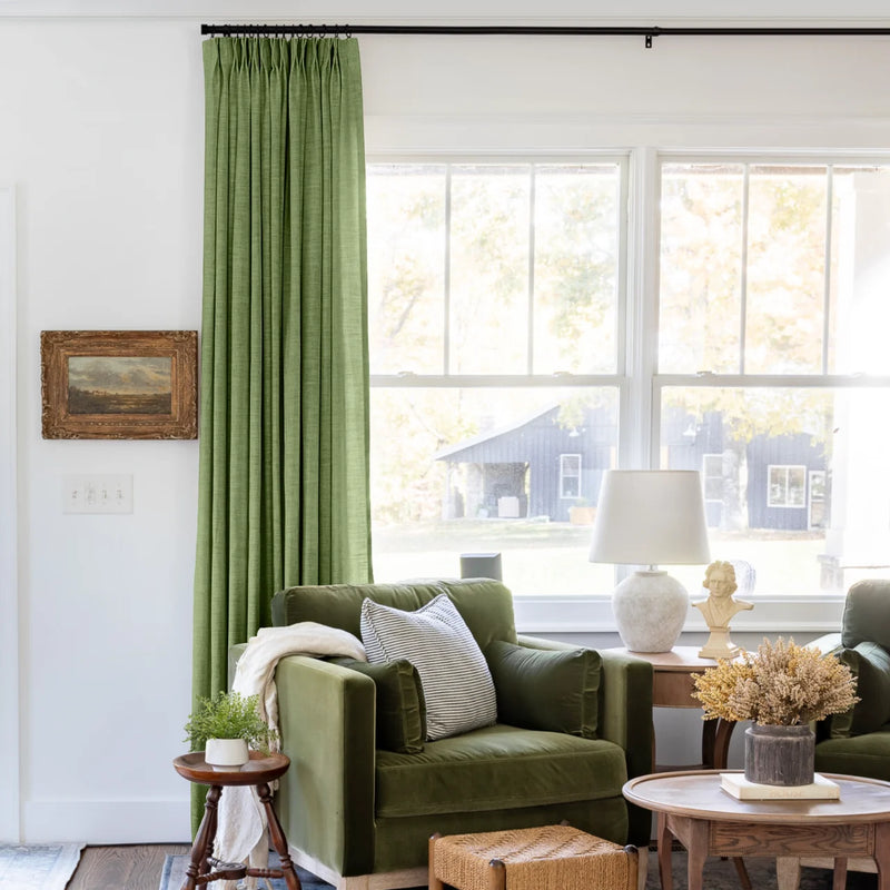 Green Liz linen curtains shown closer beside a sunlit window with smooth vertical folds