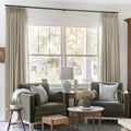 Grey Beige Liz Linen Pleated Curtains framing a green sofa beneath a wide sunlit window