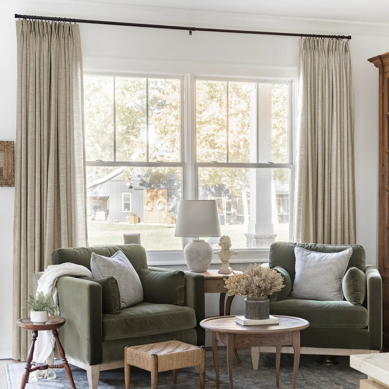 Grey Beige Liz Linen Pleated Curtains framing a green sofa beneath a wide sunlit window
