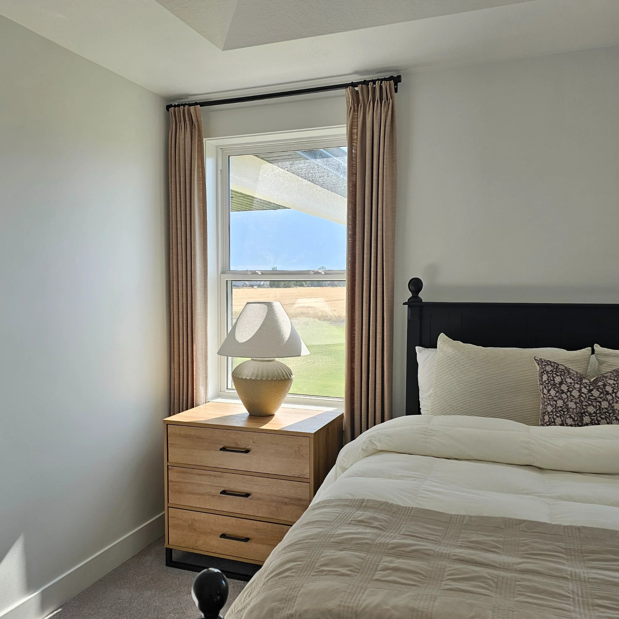 Grey Beige Liz Linen Pleated Curtains in a bedroom beside a black headboard and wooden bedside chest