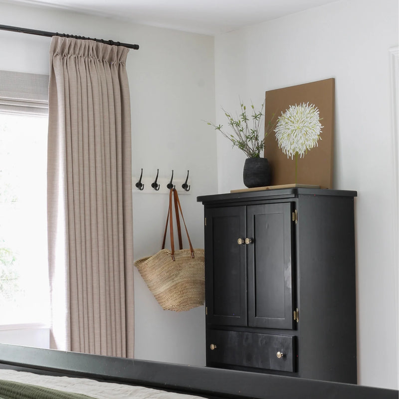 Grey Beige Liz Linen Pleated Curtains in an entryway beside a black cabinet, wall hooks and woven bag