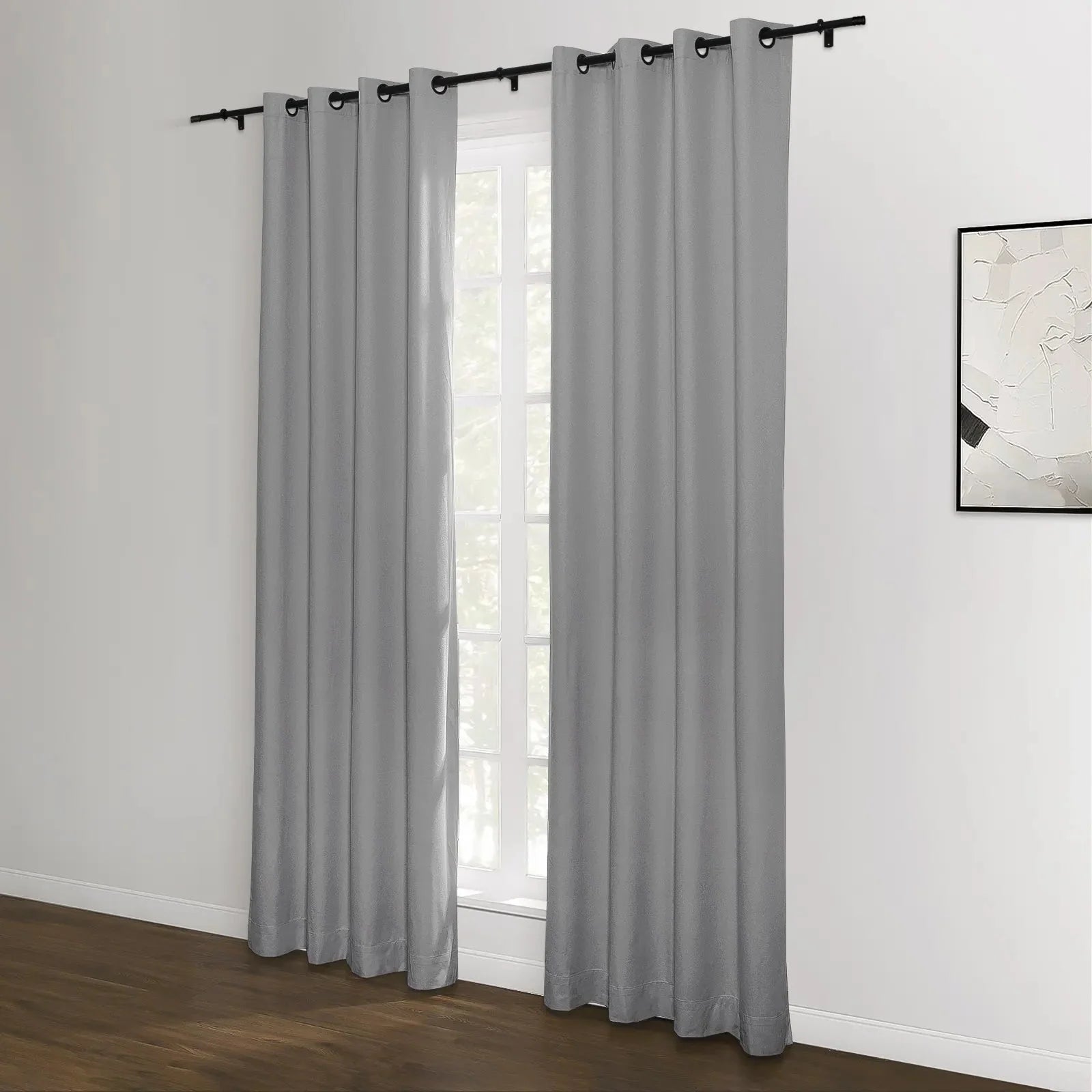 Grey grommet top blackout curtains on a black rod frame a white window in a modern room featuring dark hardwood floors and an abstract black and white artwork