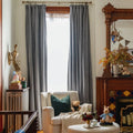 A cozy, brightly lit home interior featuring a striped armchair with an emerald green pillow, a wooden fireplace adorned with blue and yellow patterned tiles, and a unique golden bird sculpture beside a stack of children's books