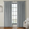 A modern interior room showcasing elegant grey pleated velvet curtains on a black rod flanking a grid-paned window, complemented by a beige armchair with a white textured throw blanket and abstract tree wall art