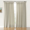 A pair of natural textured beige tab-top curtains featuring decorative bows and a black rod in a sunlit room with a small framed landscape painting