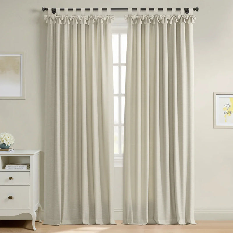 Light beige linen-look curtains with decorative tie-top tabs cover a window in a bright room featuring a white dresser with a blue vase of flowers and framed yellow inspirational artwork