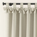 Photography of light beige linen-look tie-top curtains with decorative bows on a dark metal rod featuring a round finial and a subtle woven fabric texture