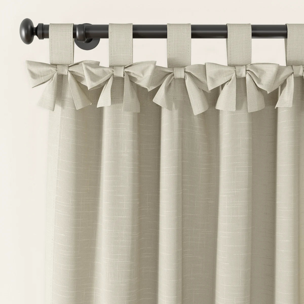 Photography of light beige linen-look tie-top curtains with decorative bows on a dark metal rod featuring a round finial and a subtle woven fabric texture