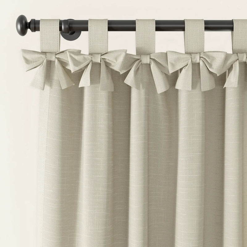 Photography of light beige linen-look tie-top curtains with decorative bows on a dark metal rod featuring a round finial and a subtle woven fabric texture