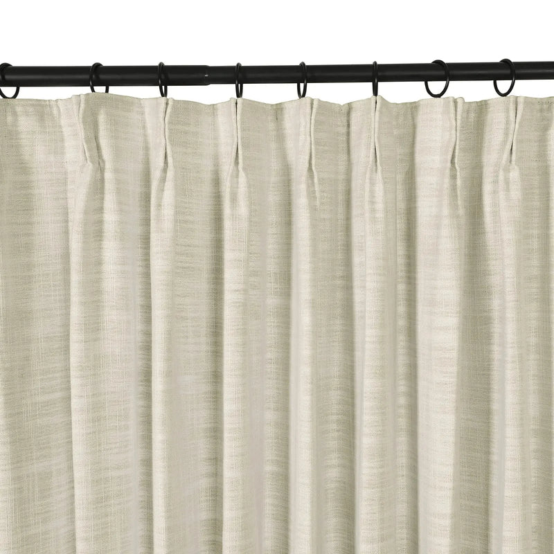 A light beige linen-look pleated curtain hanging from a black rod with rings showcasing its visible woven texture