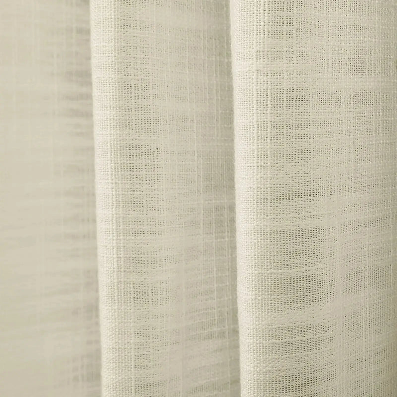 Photograph of a light beige sheer linen-look fabric curtain with prominent vertical folds and a detailed open-weave texture