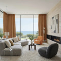 Modern beachfront living room with a light grey modular sofa, vibrant orange armchair, illuminated linear fireplace, and abstract wall art, all framed by floor-to-ceiling ocean views