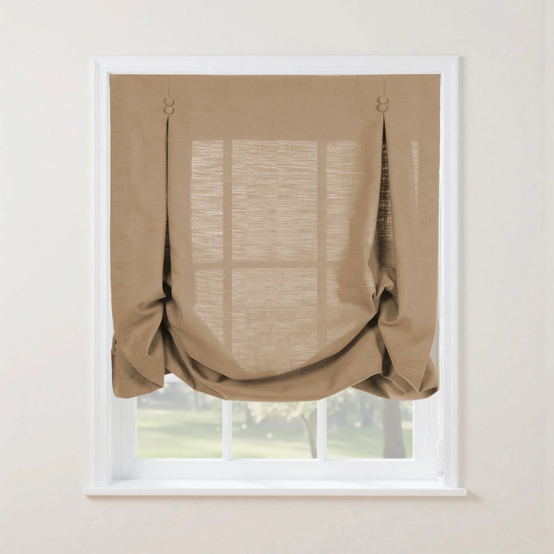 A medium brown linen-look relaxed Roman shade with two decorative button accents and soft bottom folds partially covers a white-framed window overlooking a green outdoor landscape