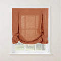 A stylish rust-orange sheer linen-blend casual balloon Roman shade with button-tab details partially covering a white-framed window looking out to a lush green garden