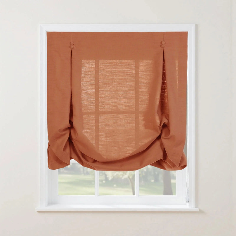A stylish rust-orange sheer linen-blend casual balloon Roman shade with button-tab details partially covering a white-framed window looking out to a lush green garden