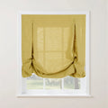 A mustard yellow textured linen relaxed Roman shade with decorative loop and button details softly draped over a white multi-pane window looking out onto a sunny green landscape