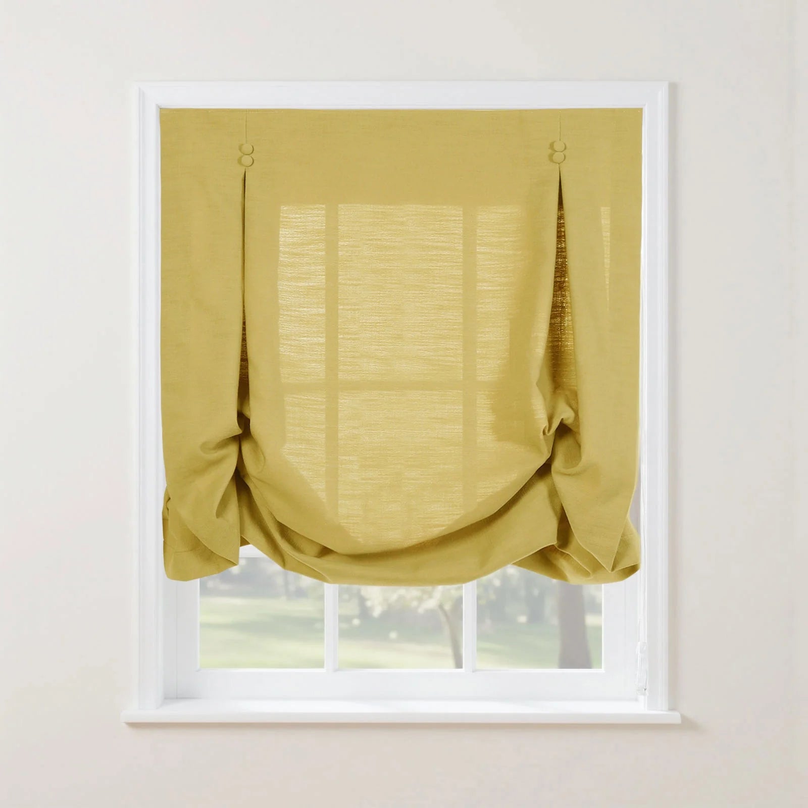 A mustard yellow textured linen relaxed Roman shade with decorative loop and button details softly draped over a white multi-pane window looking out onto a sunny green landscape