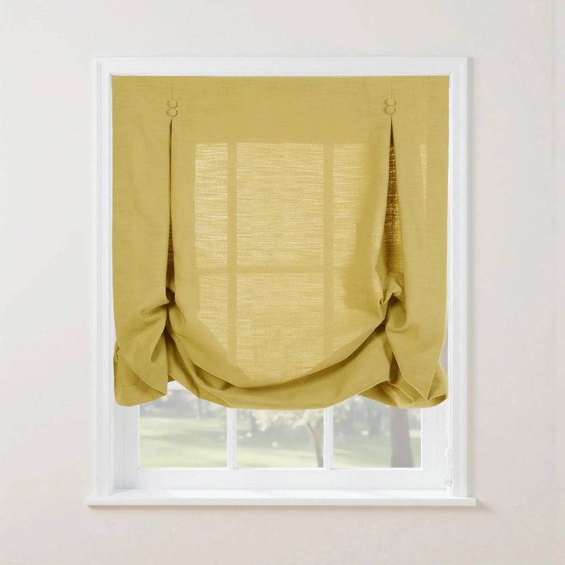 A mustard yellow textured linen relaxed Roman shade with decorative loop and button details softly draped over a white multi-pane window looking out onto a sunny green landscape