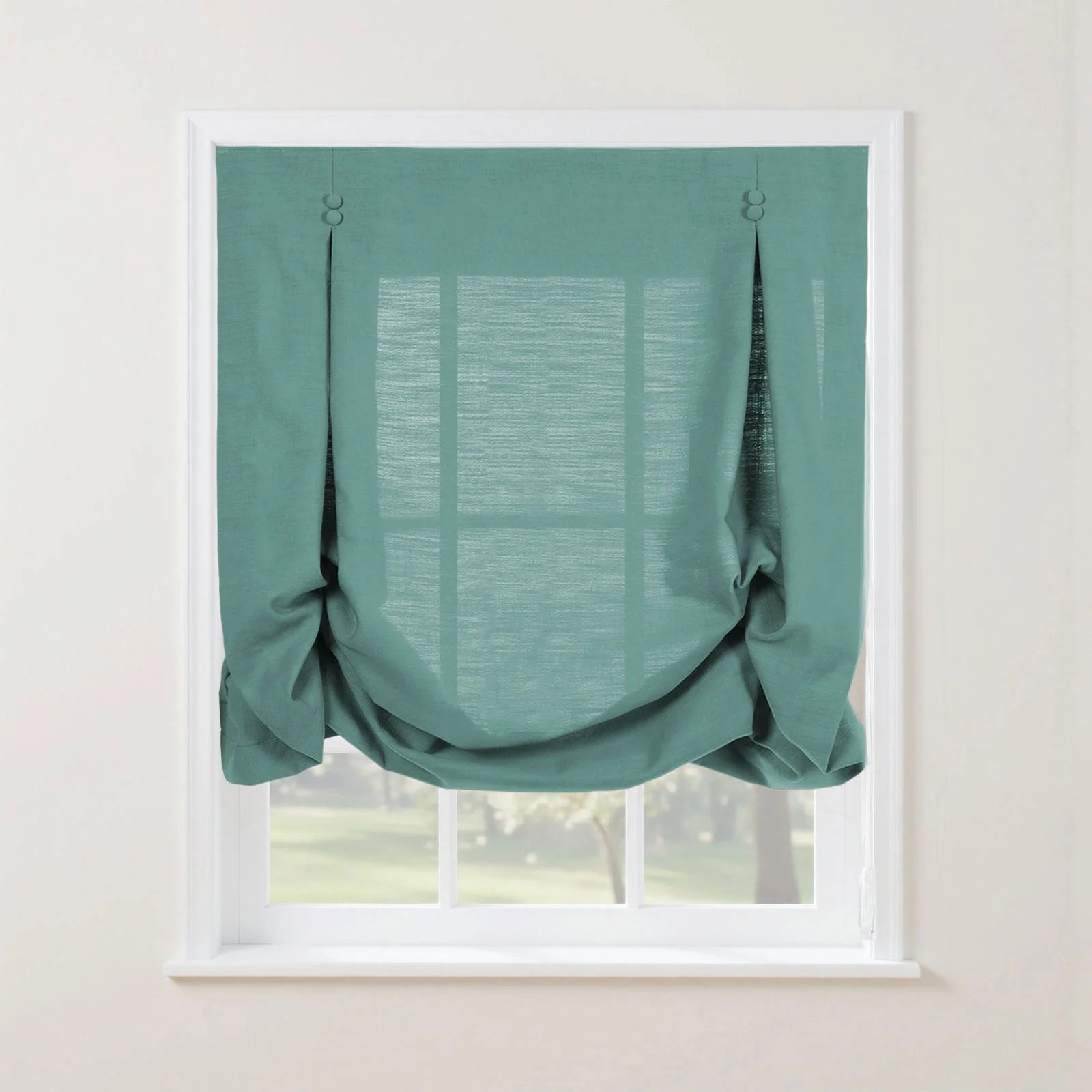 A teal linen balloon shade on a white window frame, featuring decorative buttoned pleats at the top corners and soft gathers, partially revealing a blurred green outdoor scene