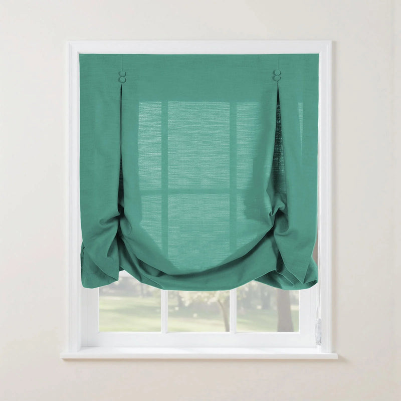 Teal linen balloon shade with decorative top loops and buttons, elegantly gathered at the bottom, covering a white-framed window overlooking a bright green garden