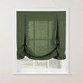 A forest green linen tie-up Roman shade with decorative button tabs and soft bottom folds partially obscures a white window frame overlooking a sunlit garden