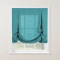 A vibrant teal textured balloon Roman shade covers a white window, featuring two decorative top buttons and soft gathers, with a blurred green garden visible beyond