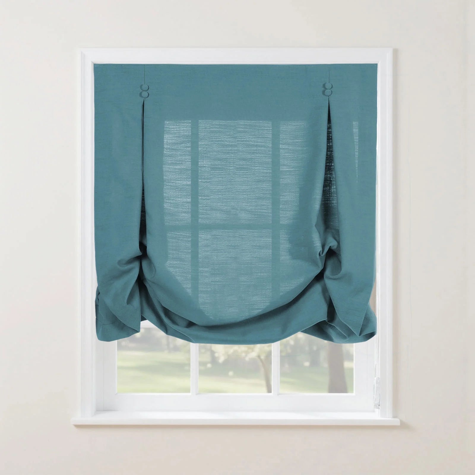 A textured teal Roman blind in a white window frame with decorative top button details and soft draping folds, overlooking a lush green garden