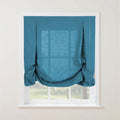 Photograph of a deep teal linen-look tie-up Roman shade with decorative button loops creating soft gathers, set in a white window frame overlooking a lush green garden