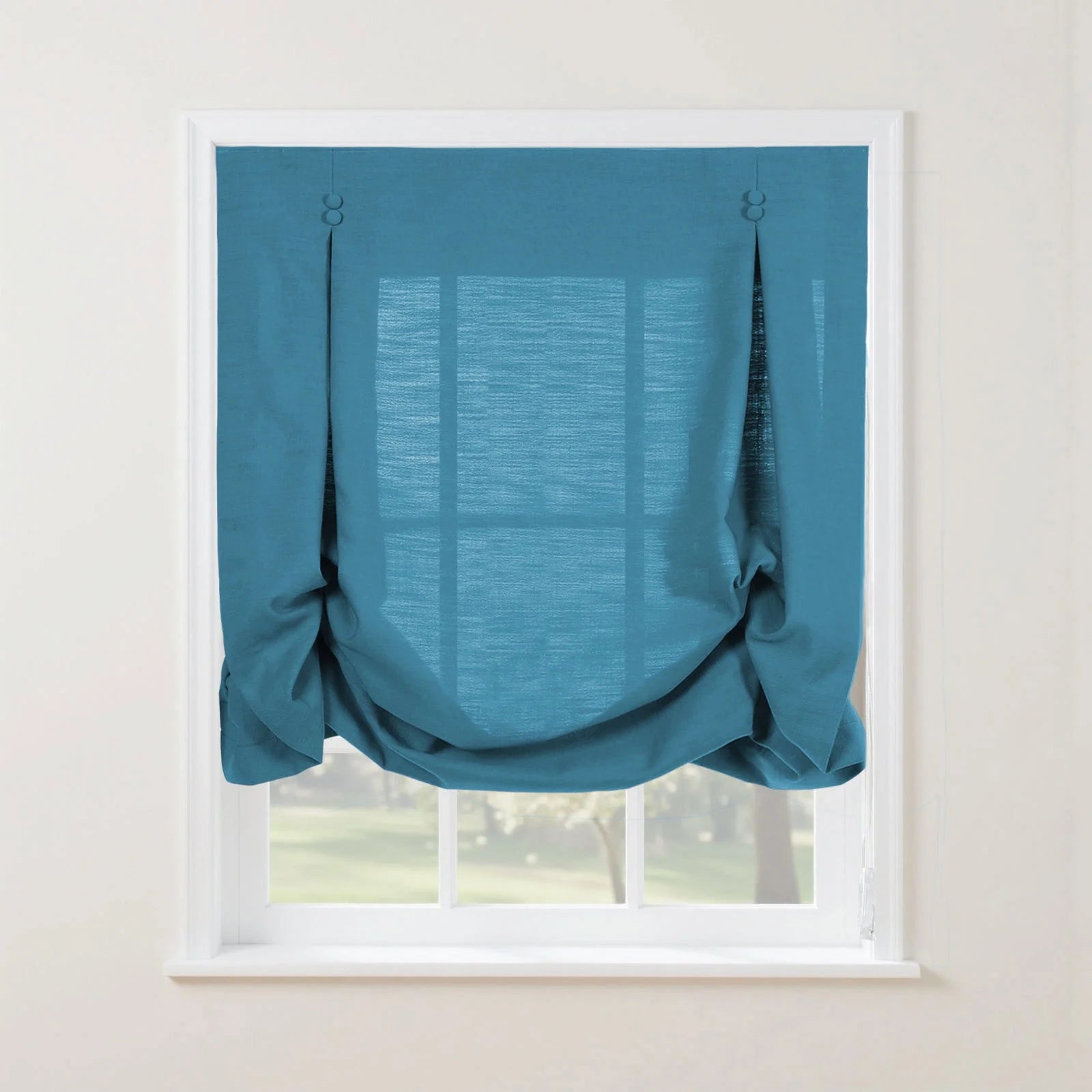 Photograph of a deep teal linen-look tie-up Roman shade with decorative button loops creating soft gathers, set in a white window frame overlooking a lush green garden
