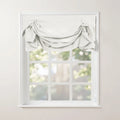 A white gathered fabric valance adorns a classic white mullioned window, offering a soft blurred view of green trees outside