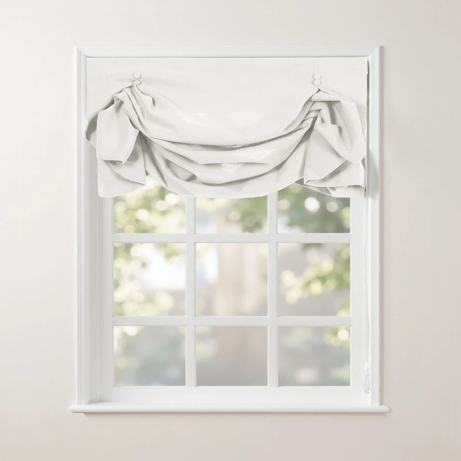 A white gathered fabric valance adorns a classic white mullioned window, offering a soft blurred view of green trees outside