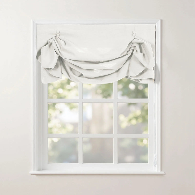 A white gathered fabric valance adorns a classic white mullioned window, offering a soft blurred view of green trees outside