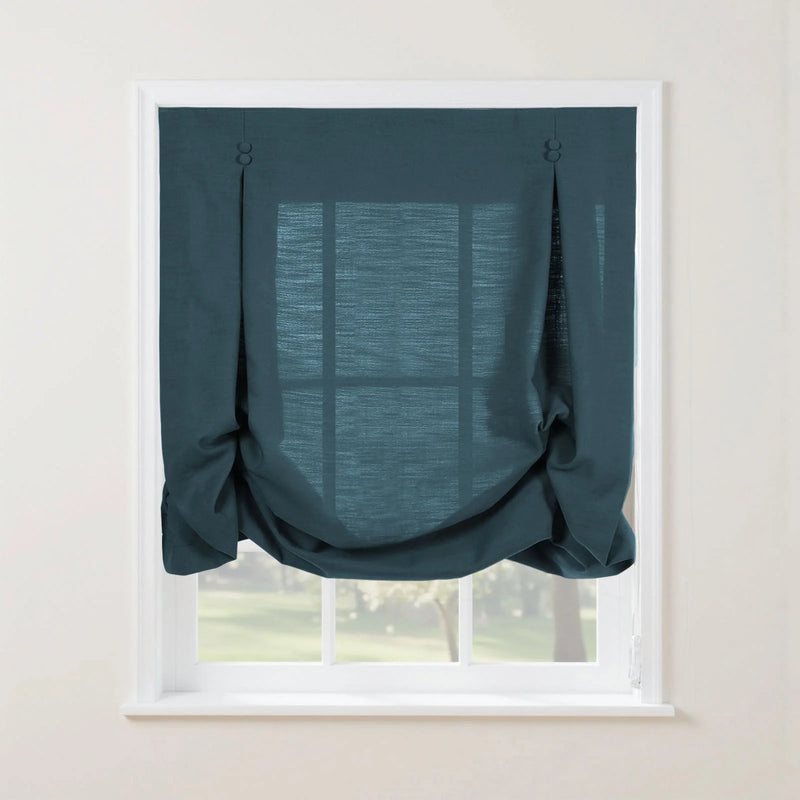 Product photography of a teal relaxed Roman window shade with decorative buttons and soft gathers on a white window frame revealing a soft green outdoor view