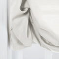 Close-up of an off-white textured linen curtain featuring soft drapes and subtle folds next to a crisp white window trim