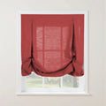 Red linen Roman blind with decorative button and loop pleats and a softly gathered bottom on a white window frame revealing a blurred green outdoor scene