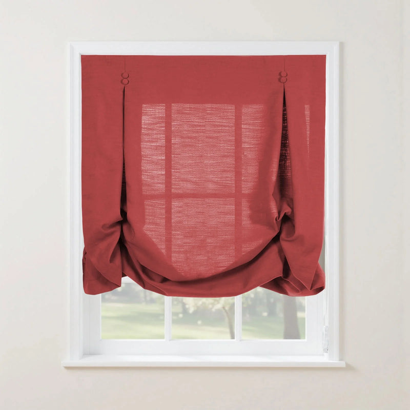 Red linen Roman blind with decorative button and loop pleats and a softly gathered bottom on a white window frame revealing a blurred green outdoor scene