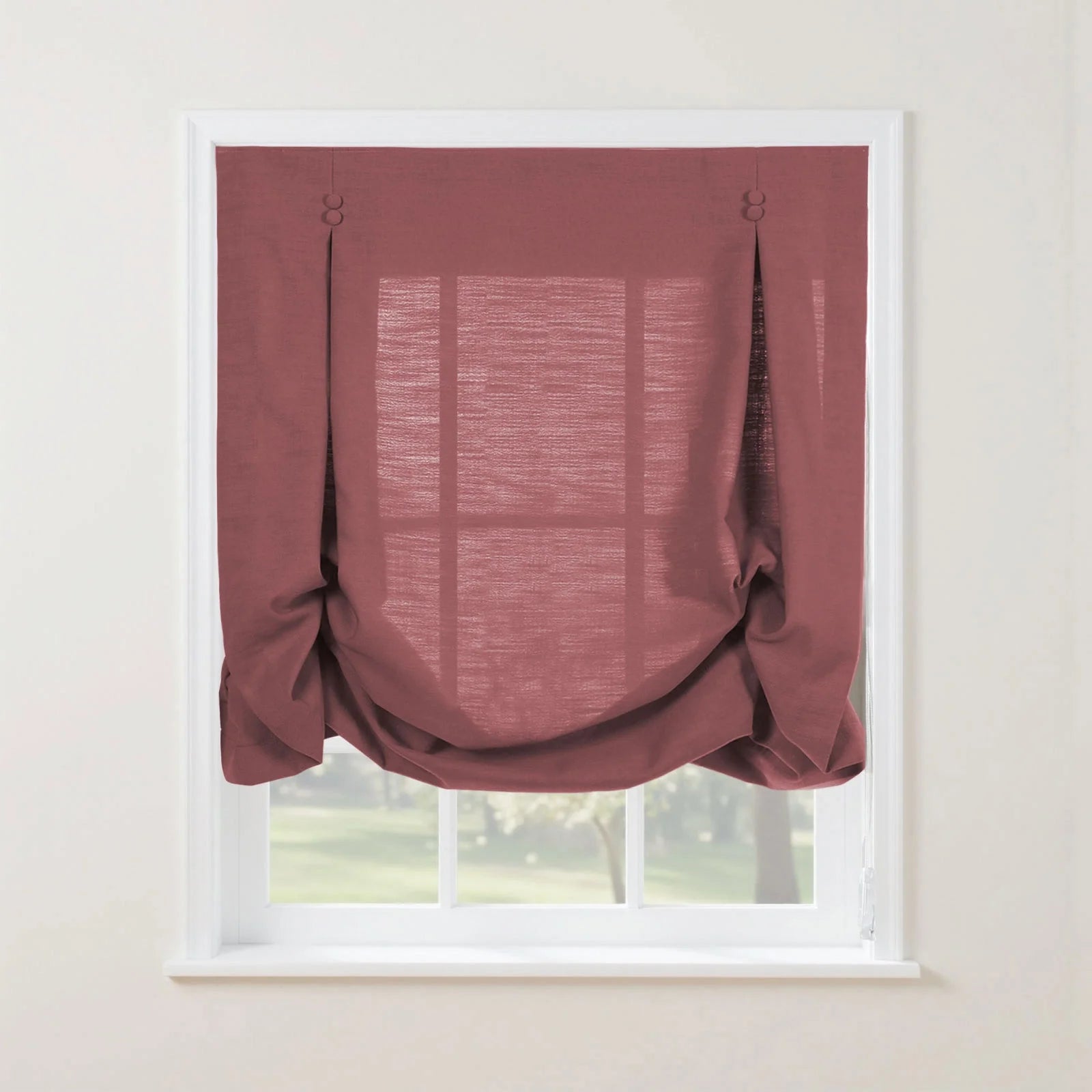 Dusty rose textured Roman window shade featuring button-loop tabs and soft gathered folds, revealing a blurred green outdoor landscape through its window panes