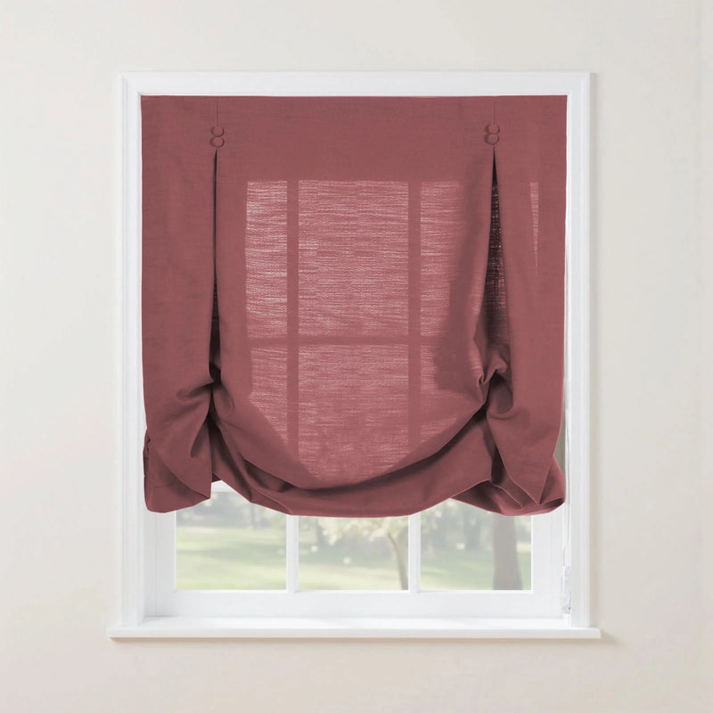 Dusty rose textured Roman window shade featuring button-loop tabs and soft gathered folds, revealing a blurred green outdoor landscape through its window panes